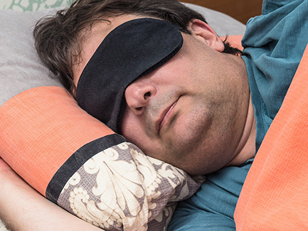 1029360818 Man sleeping with an orange blanket and wearing a sleep mask.